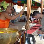 A buddhist monk sprinkles holy water on a kneeling man at a religious ceremony.